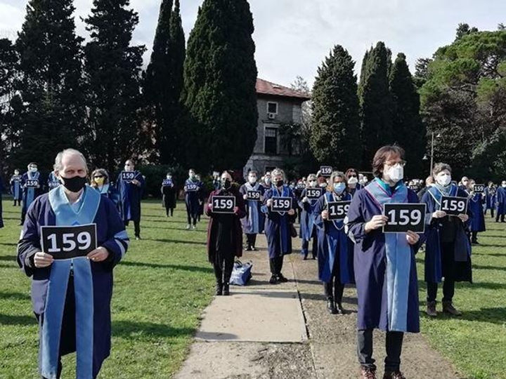 A group of academics and students outside wearing robes and facemasks and holding numbers on cards